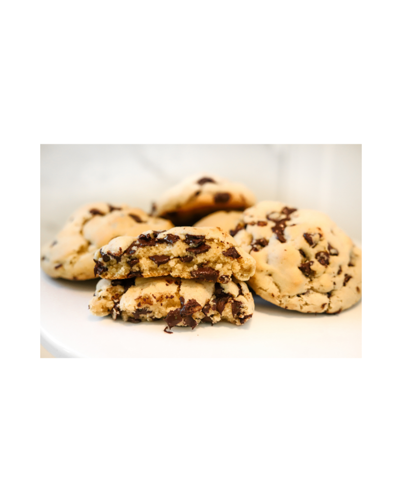 Freshly baked chocolate chip cookies stacked on a white plate, one broken open to reveal a soft chocolatey centre