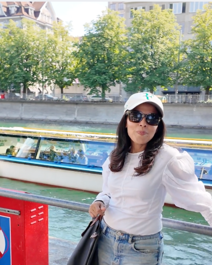 Minnal in Zurich, standing by the Limmat river on a bright summer afternoon — the quiet backdrop of her life in Switzerland.