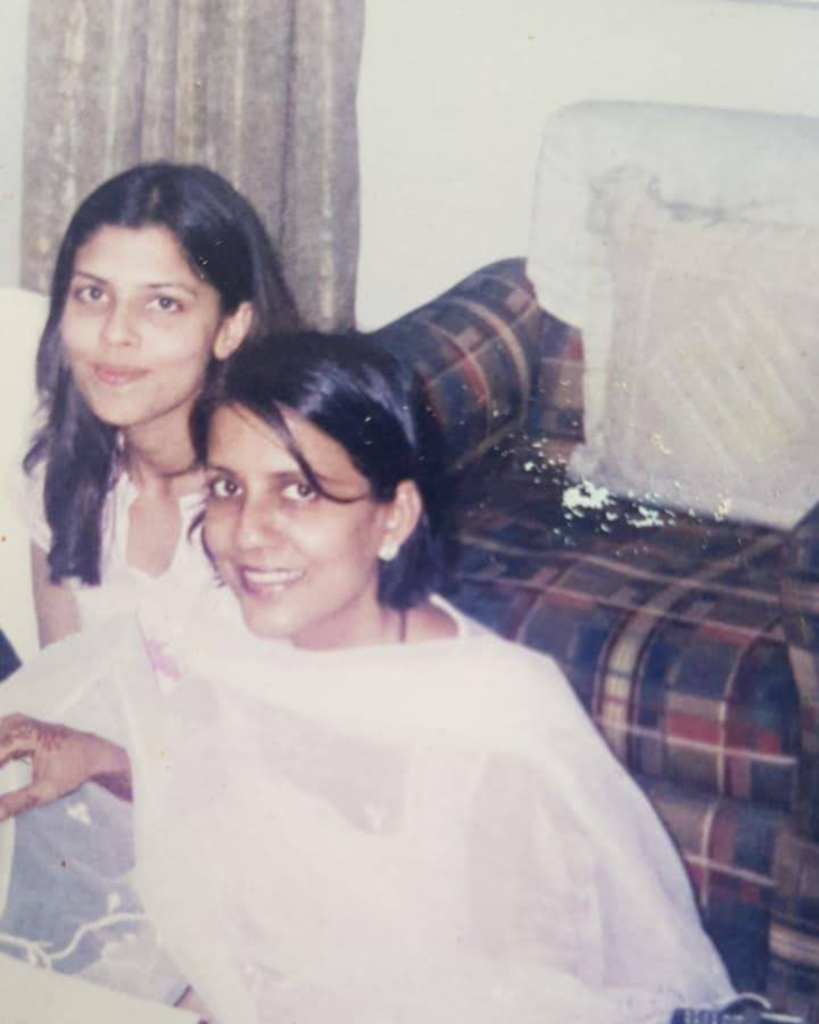 A quiet family photograph of Minnal as a young girl with her mother at home in Mumbai — softly faded, natural light.