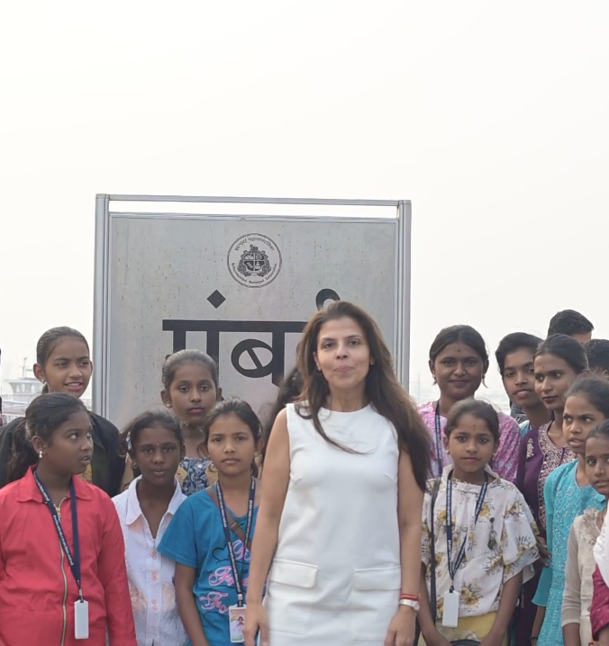 Minnal, in a white dress, standing among a group of young girls from Mumbai on a bright hazy day — supported education and mental health initiatives for low-income families.