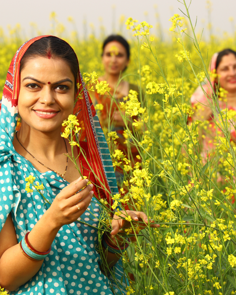 Smiling women farmers in colourful saris standing among blooming yellow mustard flowers in a sunlit Indian field